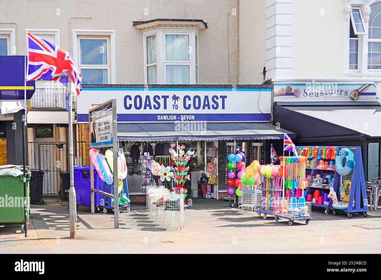 Cartello con la scritta Coast to Coast e Union Jack al negozio che espone i tipici appartamenti di villeggiatura sulla spiaggia sul marciapiede di Dawlish Devon Regno Unito Foto Stock