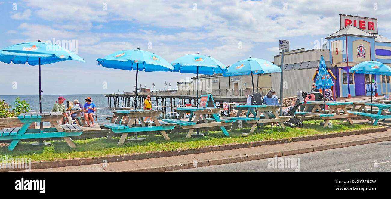 Tavoli da picnic in legno verniciati blu e panchine sul prato all'esterno, ingresso colorato e rinnovato a Teignmouth Victorian Pier Devon, Inghilterra, Regno Unito Foto Stock