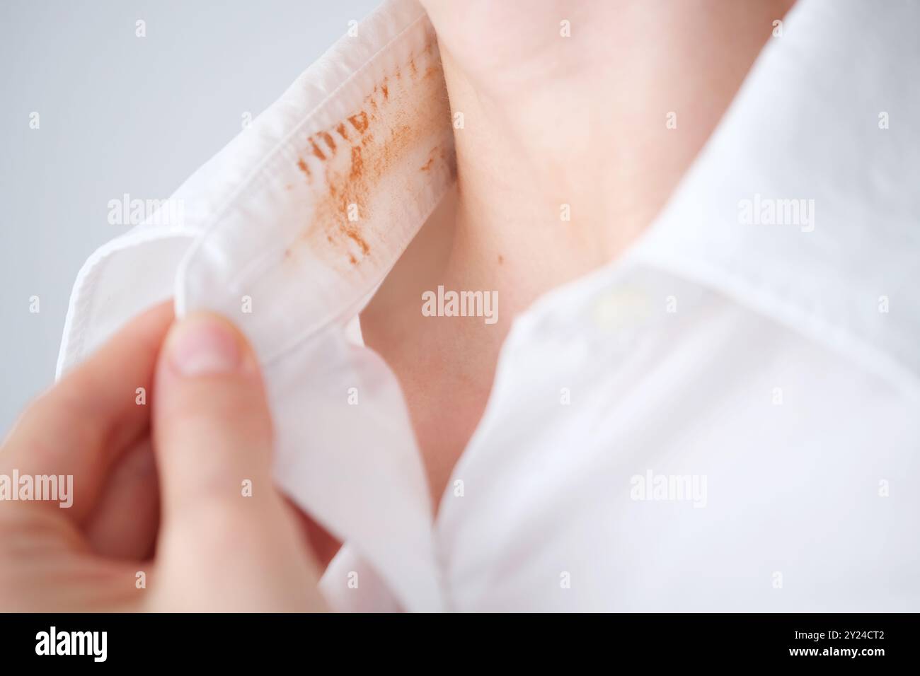 Donna senza volto che mostra una macchia cosmetica sporca sul colletto della sua camicia bianca in una stanza ben illuminata durante il giorno. concetto di colorazione per la vita quotidiana. . Alto Foto Stock