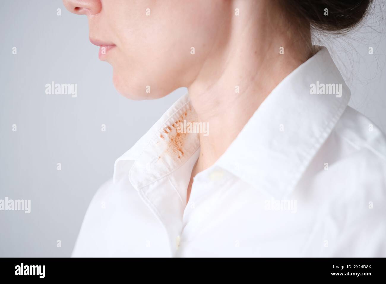 Donna senza volto che mostra una macchia cosmetica sporca sul colletto della sua camicia bianca in una stanza ben illuminata durante il giorno. concetto di colorazione per la vita quotidiana. . Alto Foto Stock