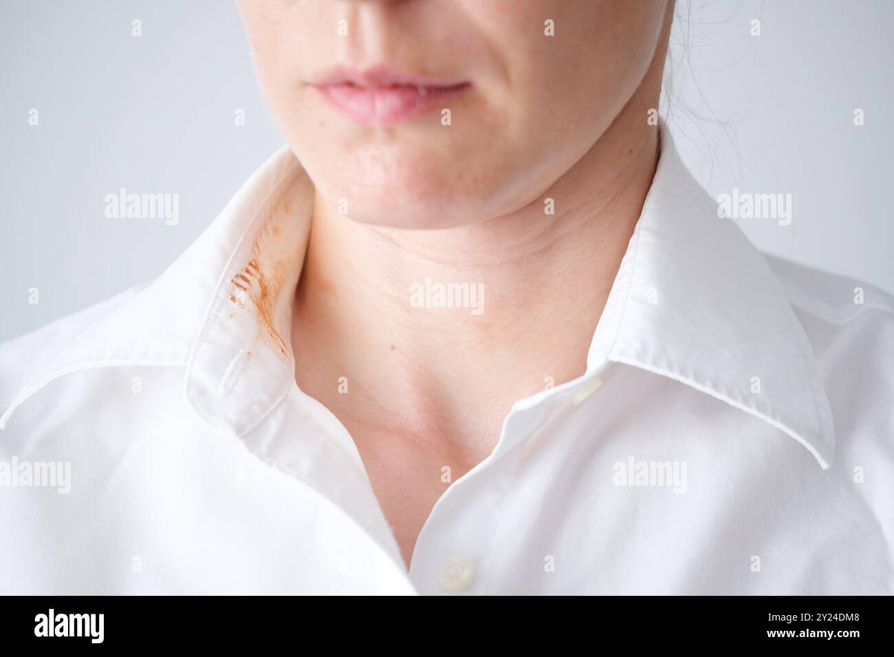 Donna senza volto che mostra una macchia cosmetica sporca sul colletto della sua camicia bianca in una stanza ben illuminata durante il giorno. concetto di colorazione per la vita quotidiana. . Alto Foto Stock