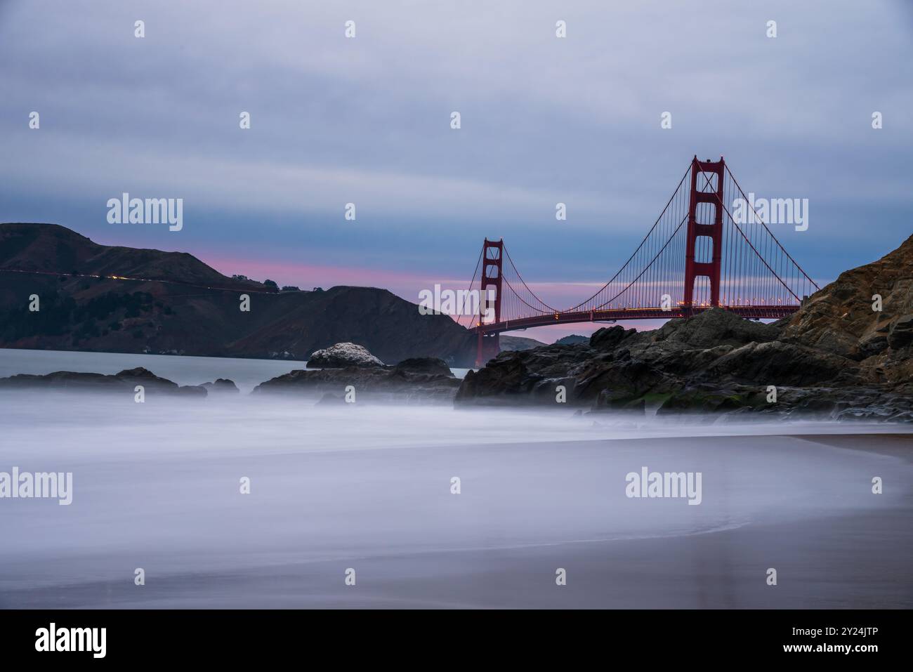 Golden Gate Bridge al crepuscolo con onde nebbiose e costa rocciosa. Foto Stock