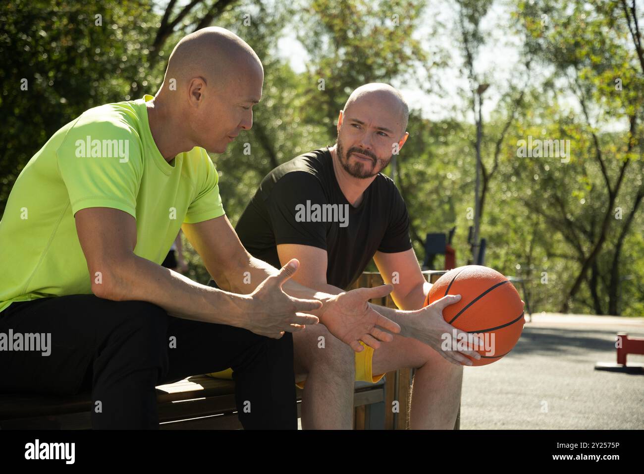Due giocatori di pallacanestro seduti sulla panchina e che discutono di una partita sul campo sportivo. Competizione sportiva. Allenamento all'aperto. Primo piano. Attività sportive. Foto Stock