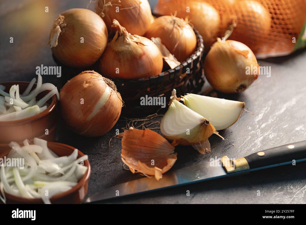 Un sacco di cipolle in un cestino e piatti su un fondo scuro ed elegante struttura scura. Foto Stock
