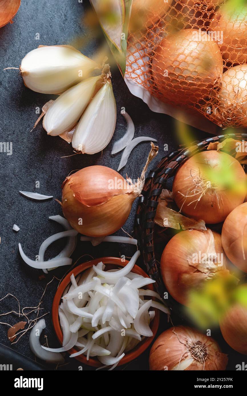 Un sacco di cipolle in un cestino e piatti su un fondo scuro ed elegante struttura scura. Foto Stock