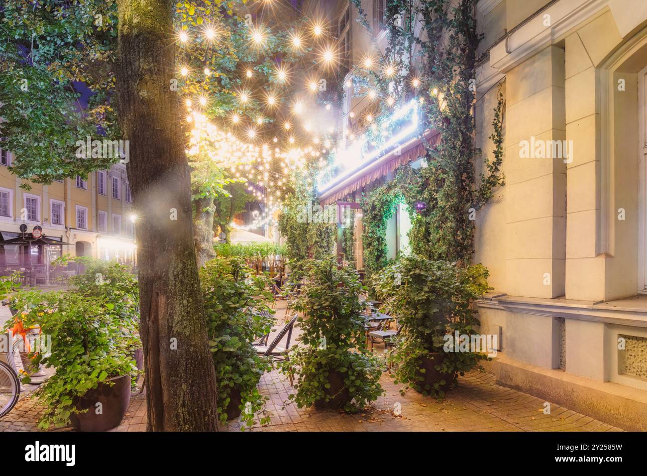 Strada della città vecchia illuminata da caldi lampioni in serata. Edifici storici, caffetterie accoglienti e gente sfocata dal movimento. Destinazioni rilassanti Foto Stock