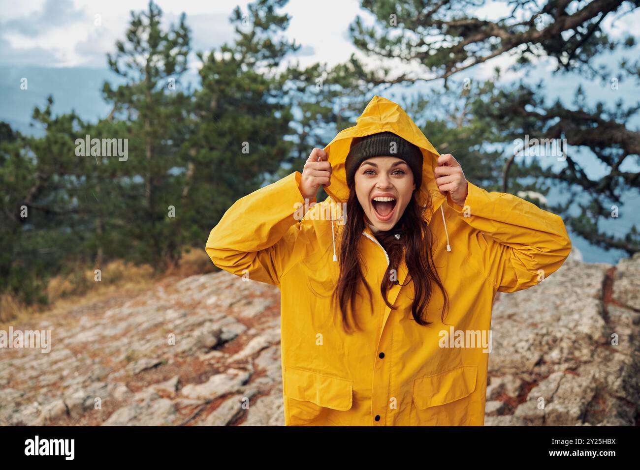 Una donna con un impermeabile giallo che si erge trionfalmente sulla cima di una maestosa vetta di montagna che si affaccia su paesaggi mozzafiato Foto Stock