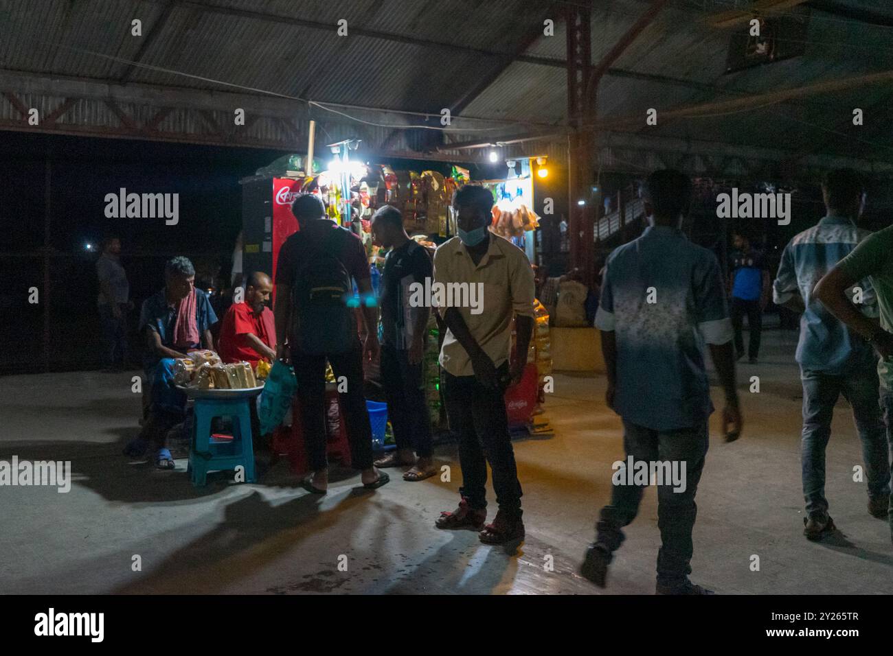 mercato notturno con venditori e acquirenti sotto l'illuminazione artificiale che crea un'atmosfera vivace. Stazione ferroviaria di Ishurdi, Bangladesh Foto Stock