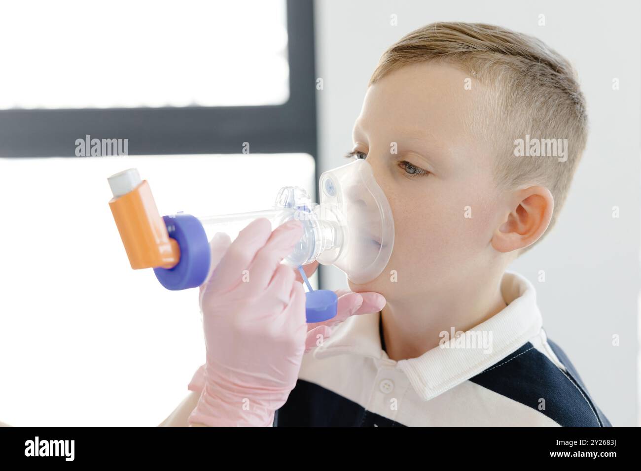 Ragazzo con asma allergica, inalando il farmaco attraverso Spacer mentre è seduto nell'ufficio medico. Foto Stock