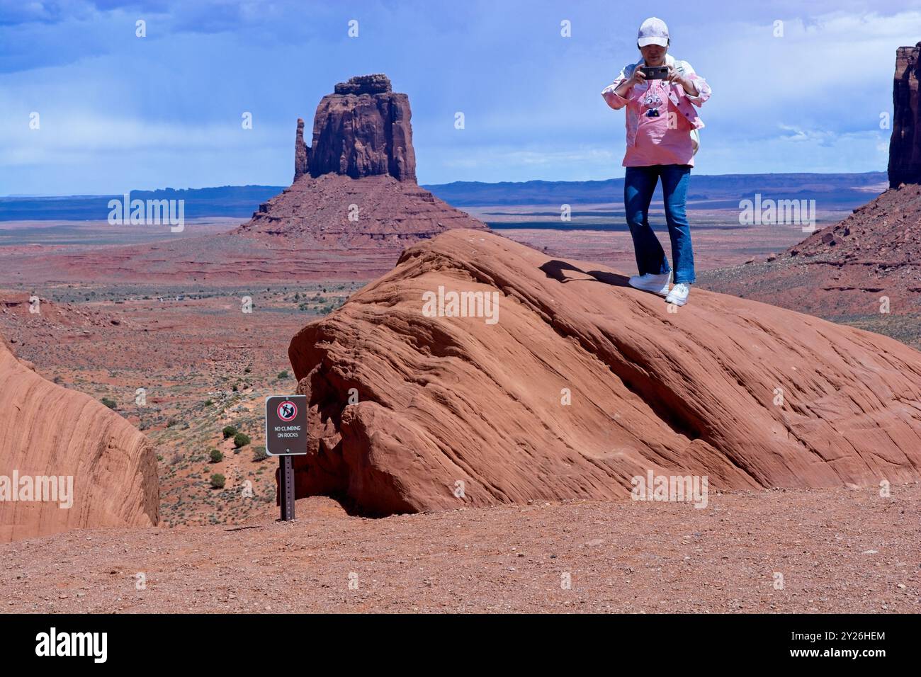 Turista in piedi su affioramento roccioso accanto al cartello "no climbing on Rocks" nella Monument Valley -- Arizona, aprile 2024 Foto Stock