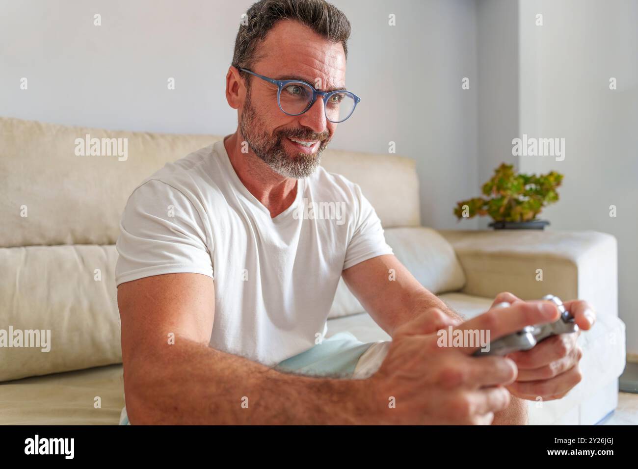 Uomo di mezza età sorridente mentre gioca ai videogiochi sul divano a casa Foto Stock