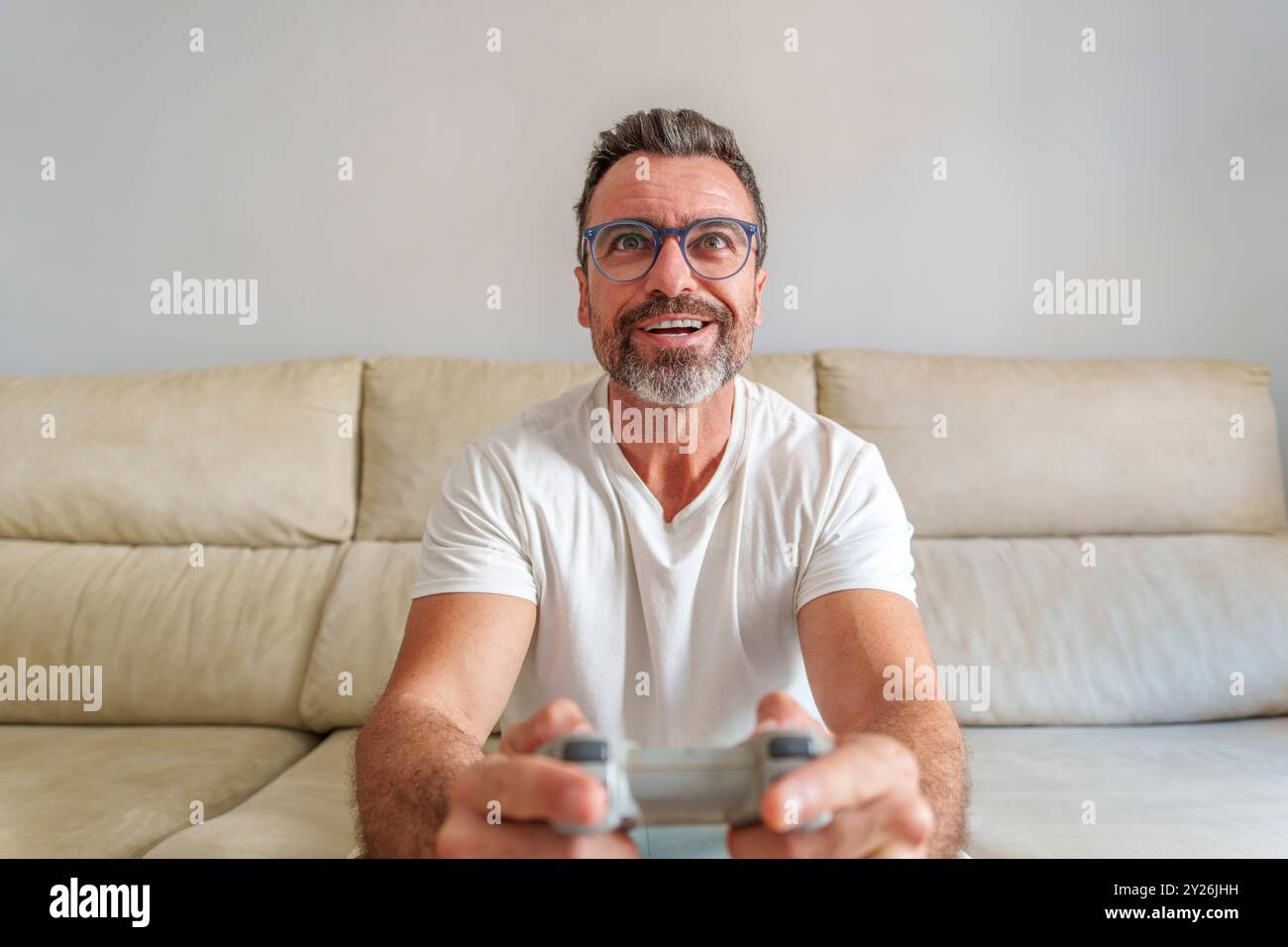 Vista frontale dell'uomo di mezza età sorridente mentre giochi ai videogiochi sul divano a casa Foto Stock