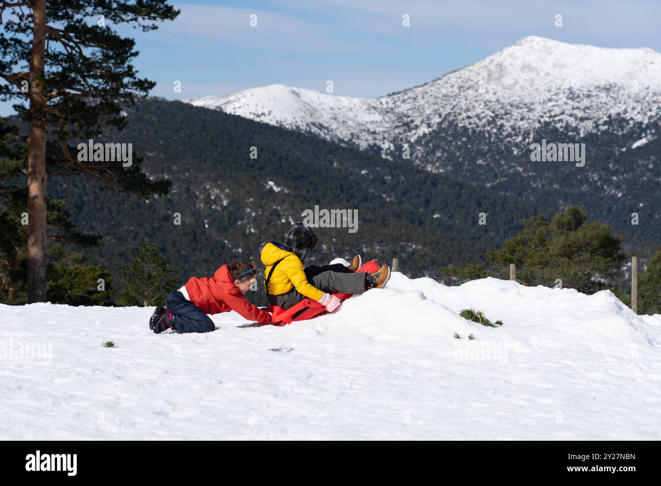 Due bambini caucasici che giocano con una slitta tra le montagne innevate in natura Foto Stock