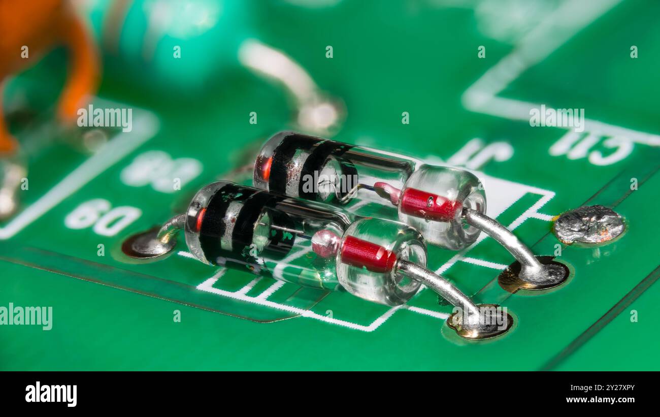 Due diodi al germanio con contatto a punti in contenitore in vetro su scheda a circuito stampato verde. Primo piano dei componenti elettronici in un tubo a strisce su un dettaglio PCB. Foto Stock