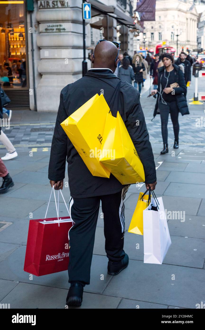 Il concetto di shopping a Londra, gli acquirenti maschi contrastano la vista dell'uomo con le numerose borse colorate che si trovano a pochi passi da Regent Street, Londra, Inghilterra, Regno Unito Foto Stock