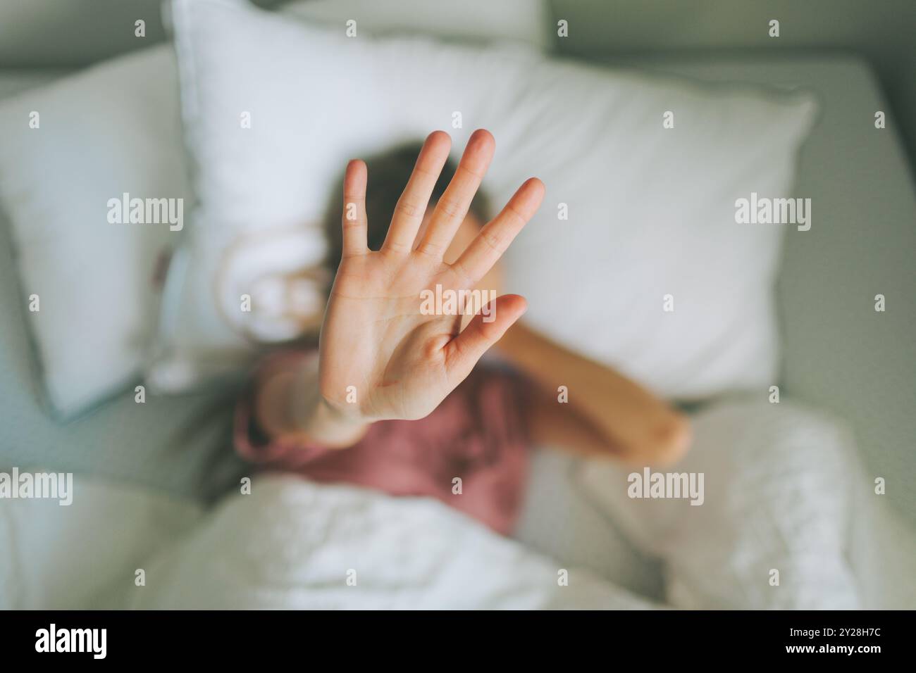 Una donna a letto tiene la mano in alto per coprire il viso. Foto Stock