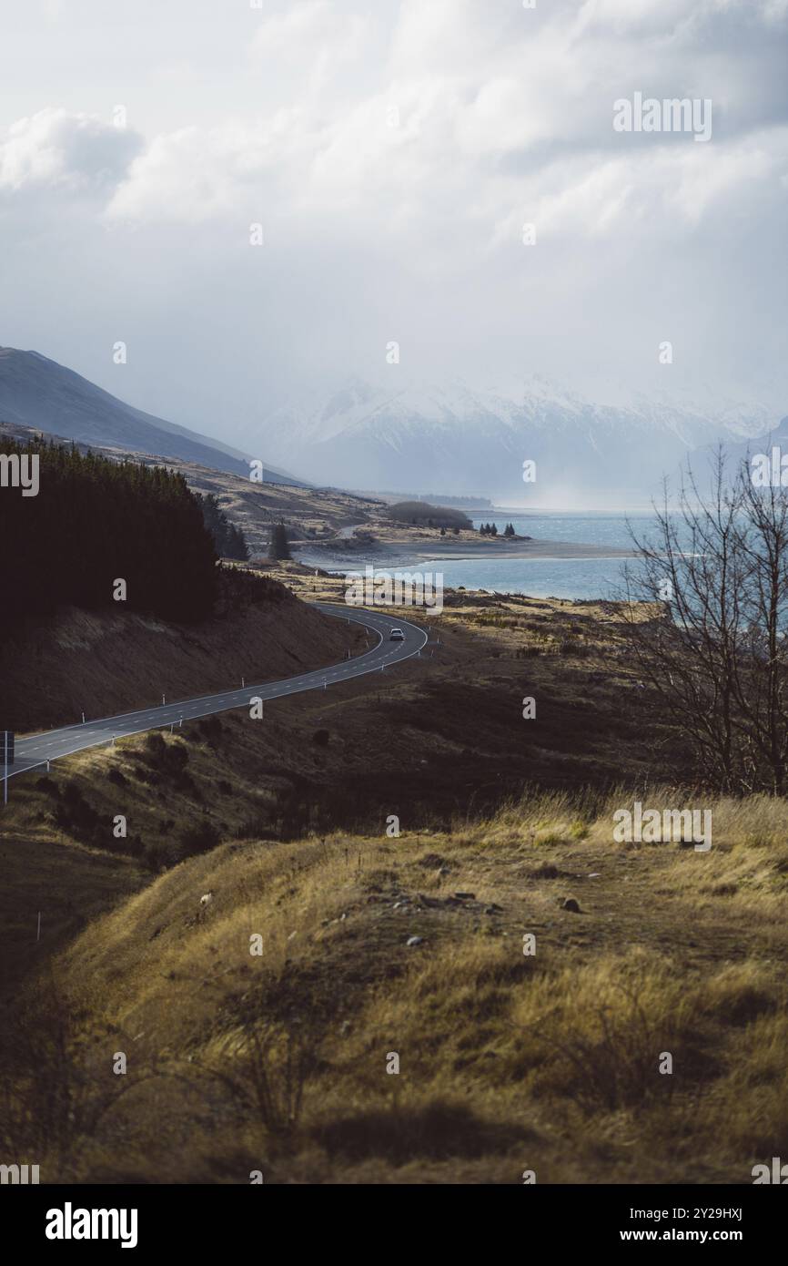 Strada che conduce lungo un lago con colline boscose e montagne sullo sfondo sotto un cielo nuvoloso, Hooker Valley Track, nuova Zelanda, Oceania Foto Stock