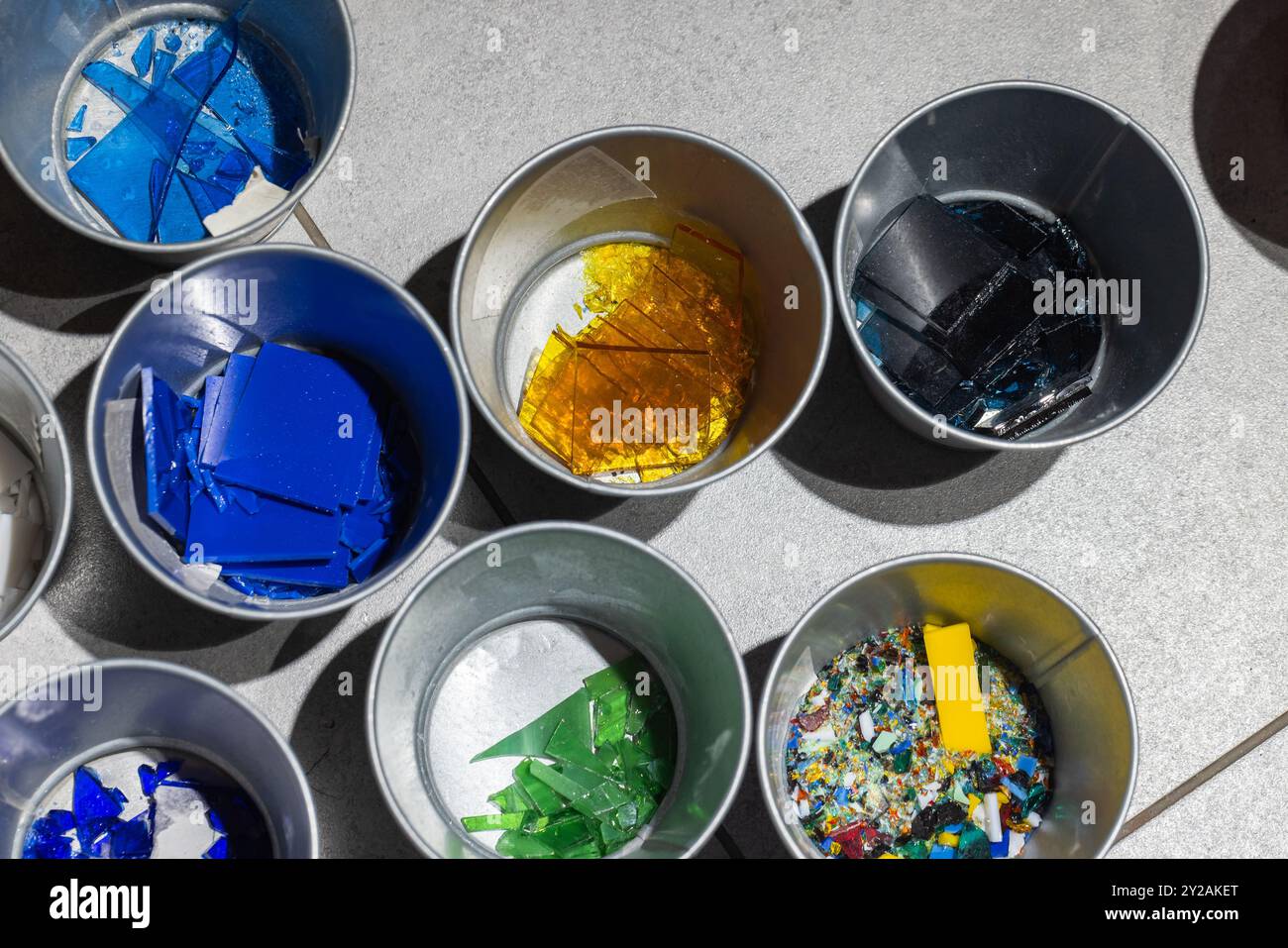 I frammenti di vetro colorati per la fusione vengono ordinati in piccoli contenitori metallici, foto ravvicinata con messa a fuoco selettiva Foto Stock