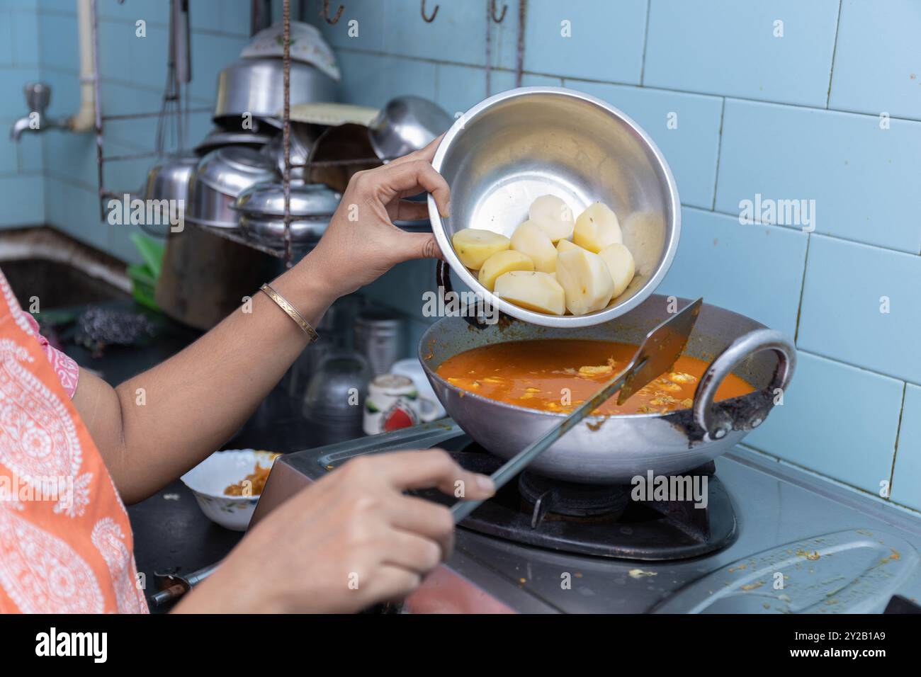 Il curry di pollo piccante indiano viene cucinato e le patate vengono aggiunte in un utensile di alluminio sul forno a gas Foto Stock