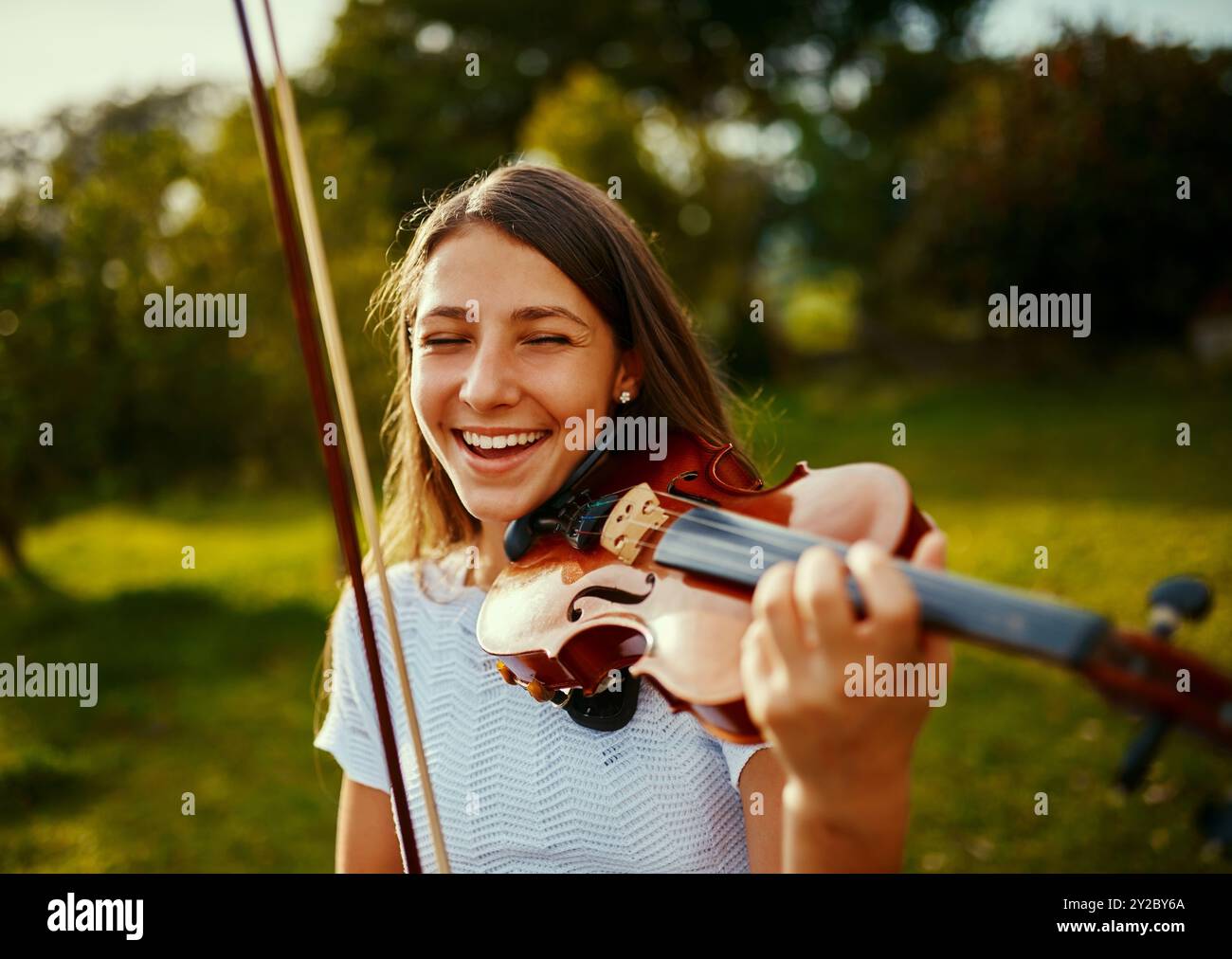 Ragazza, violino e felice in natura per musica, talento e intrattenimento per eventi. Musicista, strumento ad arco e sorridi sull'erba per l'arte, le prove e Foto Stock