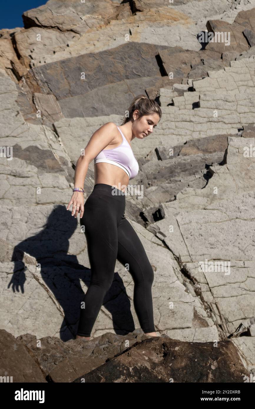 Donna in abbigliamento sportivo che scende con attenzione su terreni rocciosi, concentrata sull'avventura all'aria aperta e sulle sfide di fitness Foto Stock