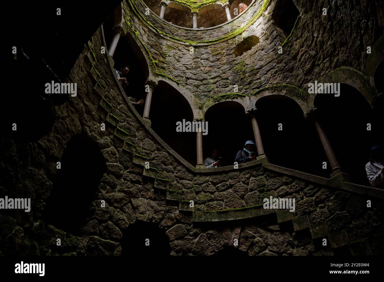 I visitatori esplorano il Pozzo Iniciático di Quinta da Regaleira, un pozzo di pietra a spirale con archi coperti di muschio e antiche murature Foto Stock