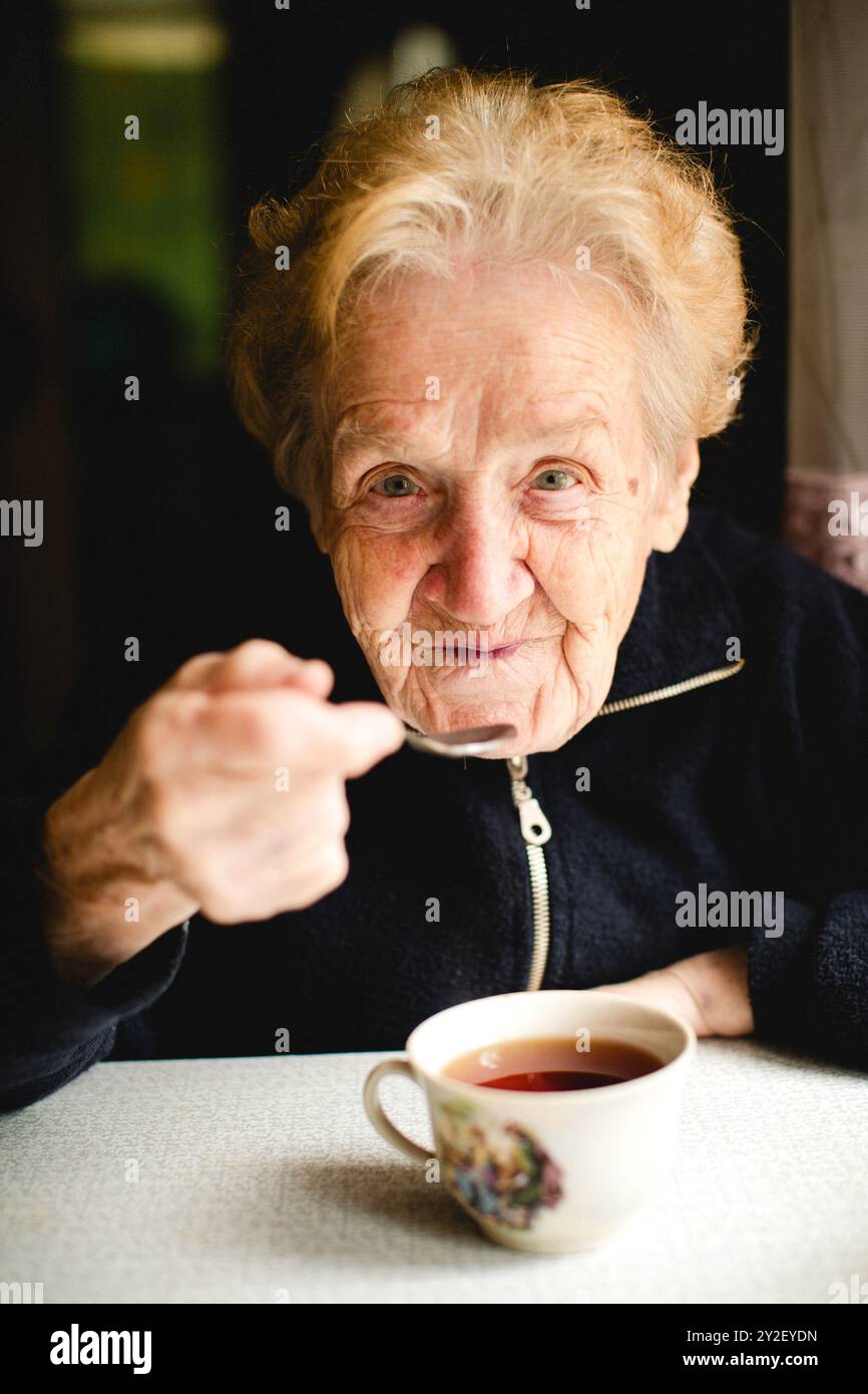 Una donna anziana siede comodamente nella sua accogliente casa, gustando una tazza di tè caldo. Foto Stock