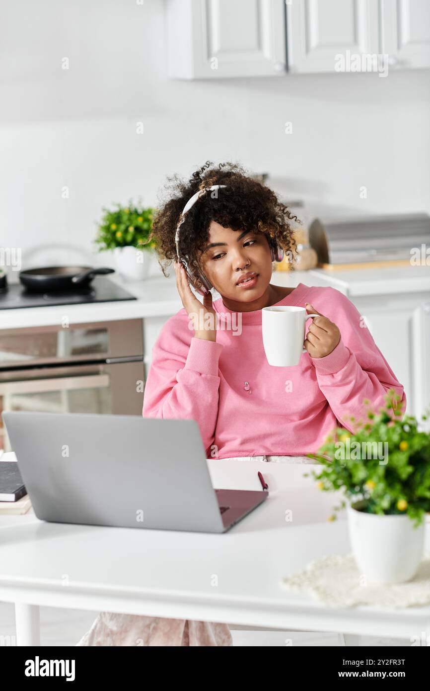 Una giovane donna gode di un momento accogliente a casa con un caffè e un laptop. Foto Stock