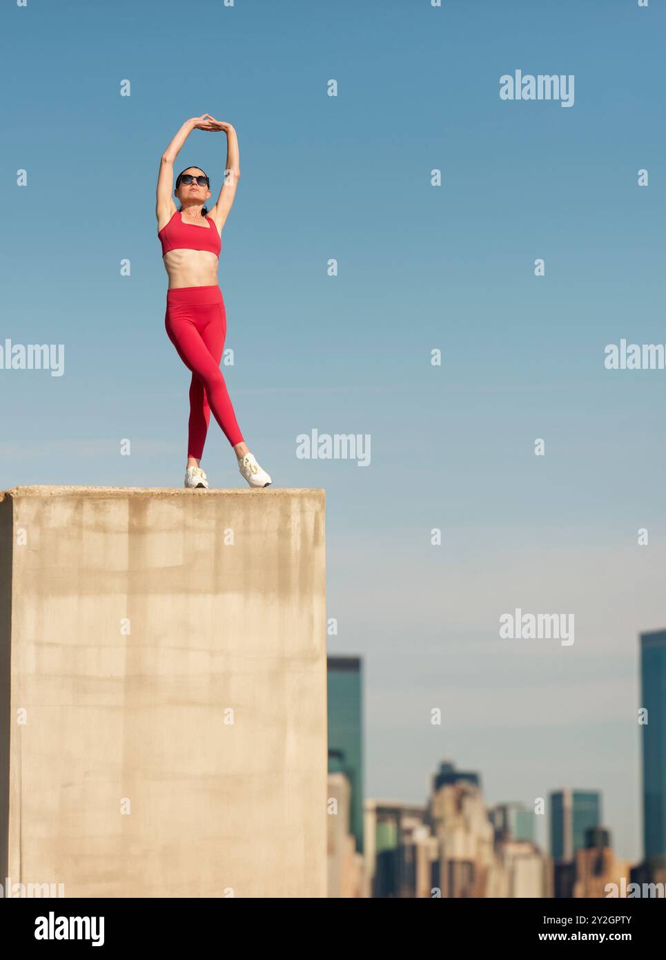 Donna sportiva che fa un esercizio di stretching del braccio in piedi in cima a un edificio alto sopra una città Foto Stock