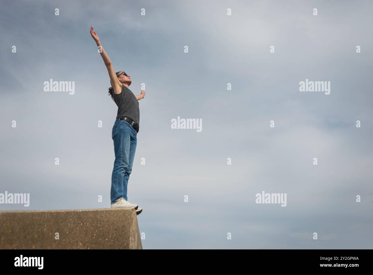 Donna in piedi in cima a un edificio in cemento con le braccia alzate per festeggiare, concetto di felicità Foto Stock