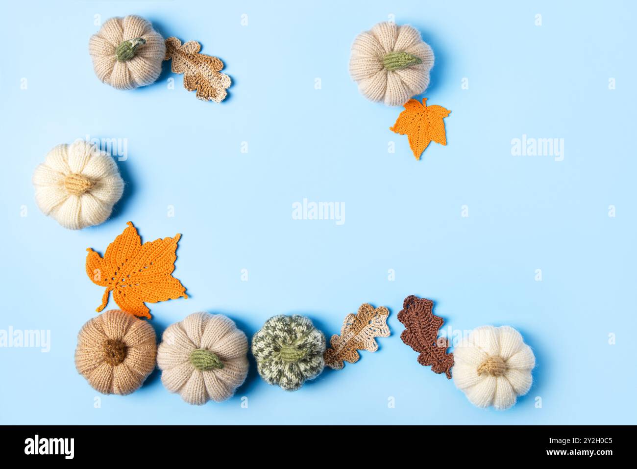 Composizione autunnale di giocattoli a maglia a forma di foglie di quercia e acero, zucche beige su sfondo blu. Concetto di autunno, Ringraziamento, Halloween Foto Stock