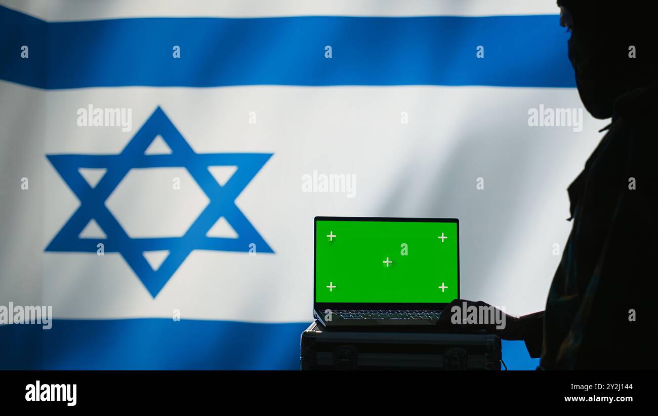 L'agente di polizia segreta di Israele utilizza strumenti di propaganda di massa su laptop con schermo verde per influenzare le menti della popolazione e diffondere disinformazione. La spia del Mossad commette il sabotaggio PsyOp utilizzando il notebook mockup, la fotocamera B. Foto Stock