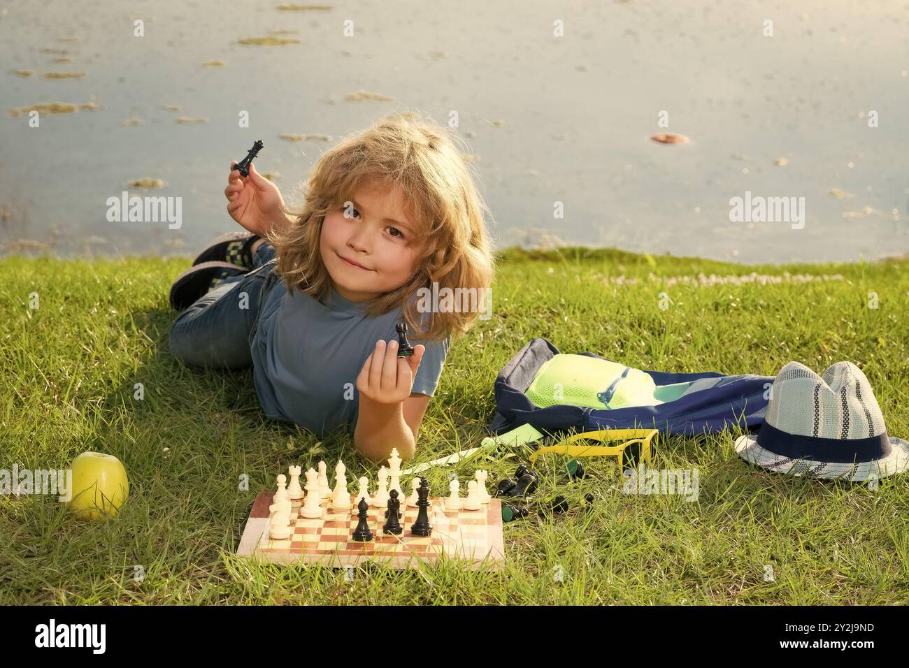 Il ragazzo mostra i pezzi degli scacchi su una scacchiera. Sviluppo precoce. Ragazzo che pensa agli scacchi nel parco estivo. Il concetto di apprendimento e crescita dei bambini. Esterno Foto Stock