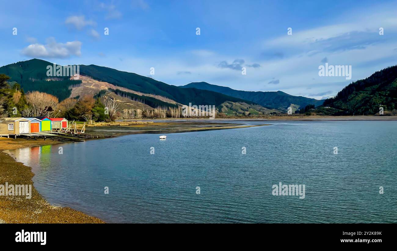 Le calme acque del Marlborough suonano con una fila di capannoni per barche dai colori vivaci sulla riva Foto Stock