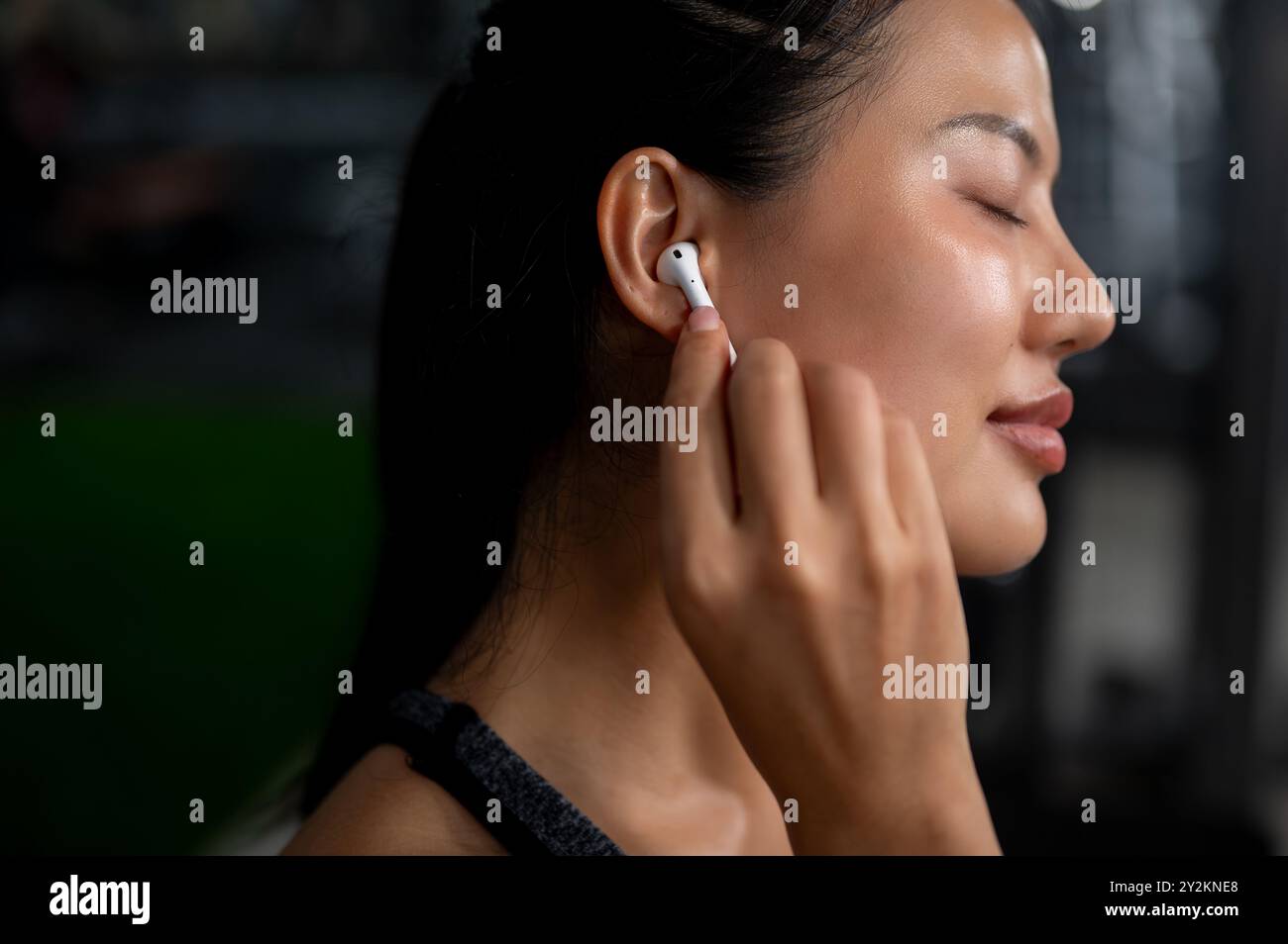 Vista ravvicinata di una bellissima donna asiatica sportiva con pelle abbronzata, occhi chiusi, musica attraverso le sue cuffie mentre si allena Foto Stock