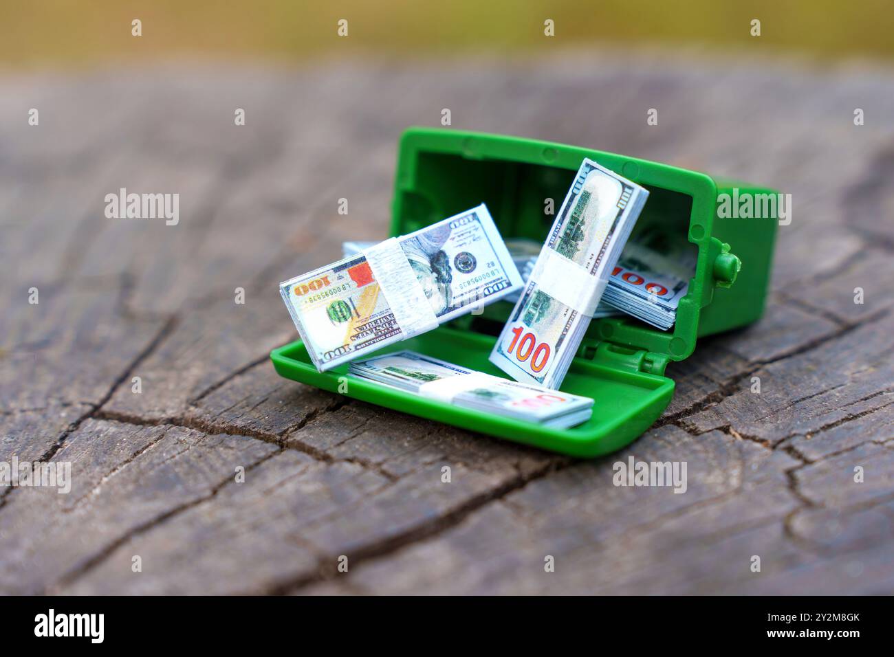 Vista ravvicinata di un bidone verde in miniatura pieno di pile di contanti, che simboleggia gli sprechi finanziari e le cattive abitudini di spesa. Foto Stock