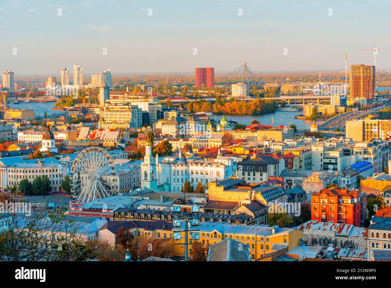 Kiev, Ucraina - 14 ottobre 2023: Vista dettagliata del quartiere di Podil a Kiev, con una ruota panoramica e un moderno skyline illuminato dalla luce del sole autunnale. Foto Stock
