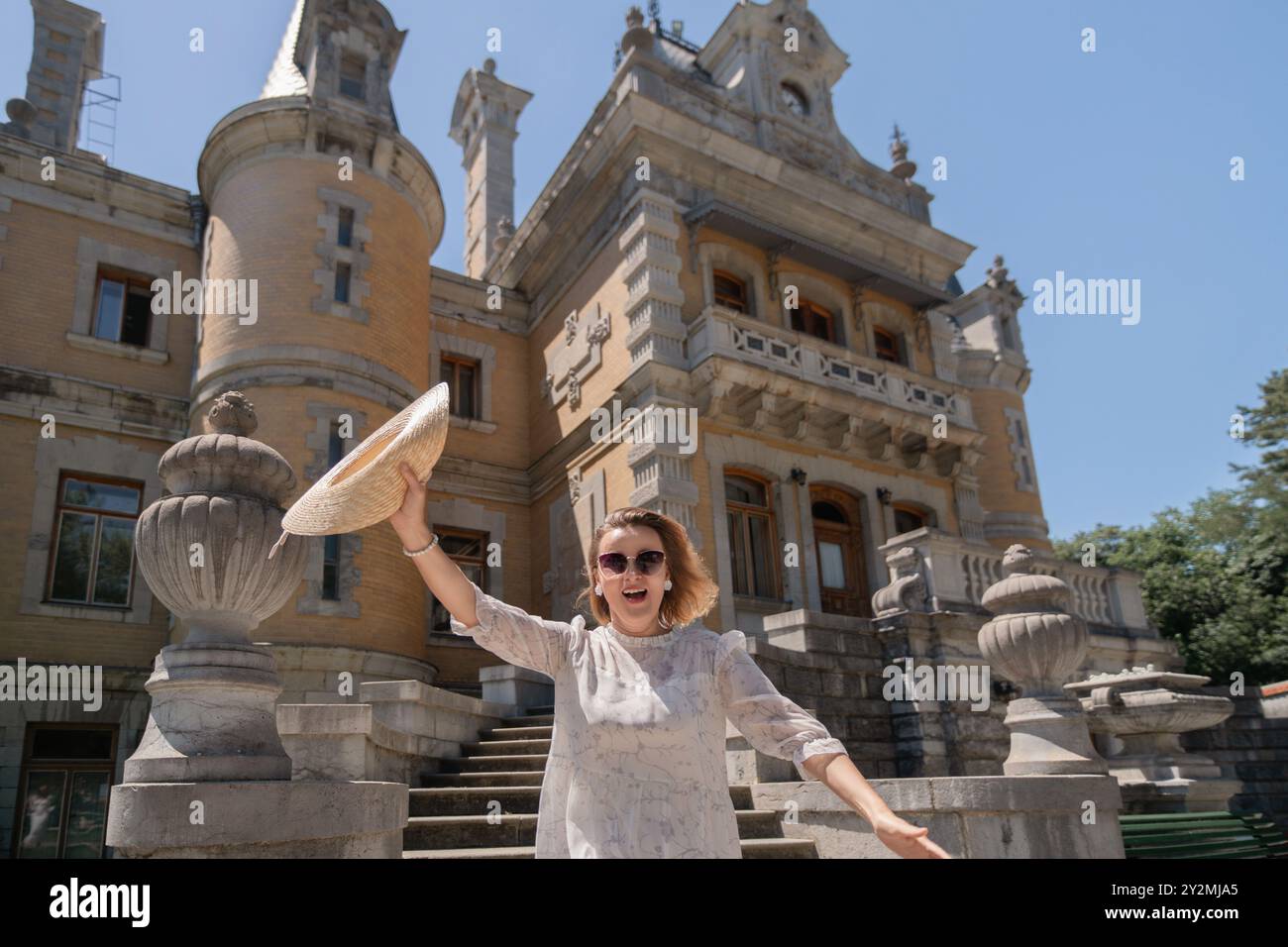 Una donna è in piedi di fronte a un grande edificio, tenendo un cappello di paglia e sorridendo. Concetto di gioia e felicità, mentre la donna si sta godendo il suo tempo libero Foto Stock