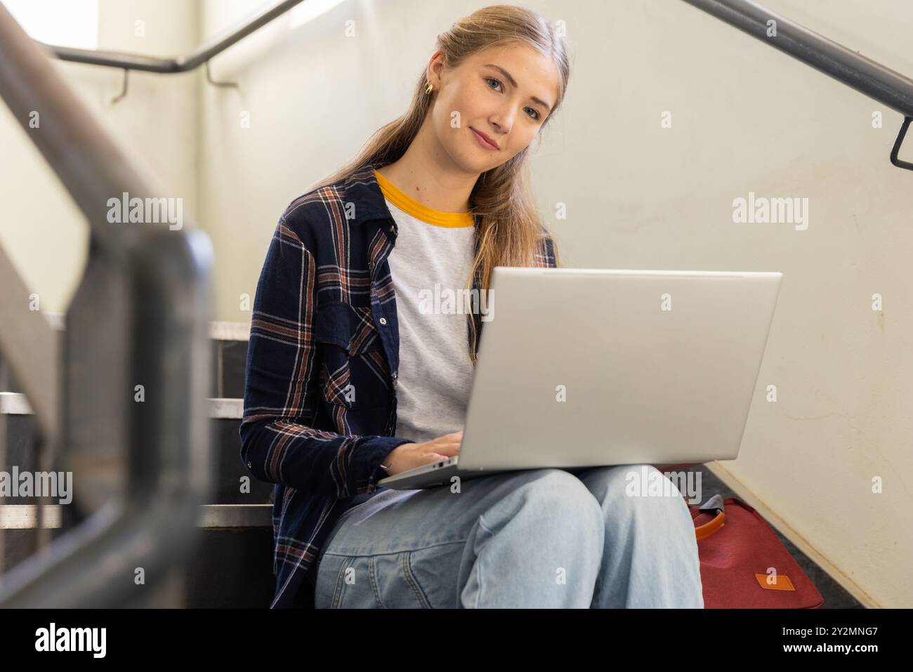 Utilizzando un computer portatile, una ragazza adolescente seduta sulle scale, che studia e si rilassa a scuola Foto Stock