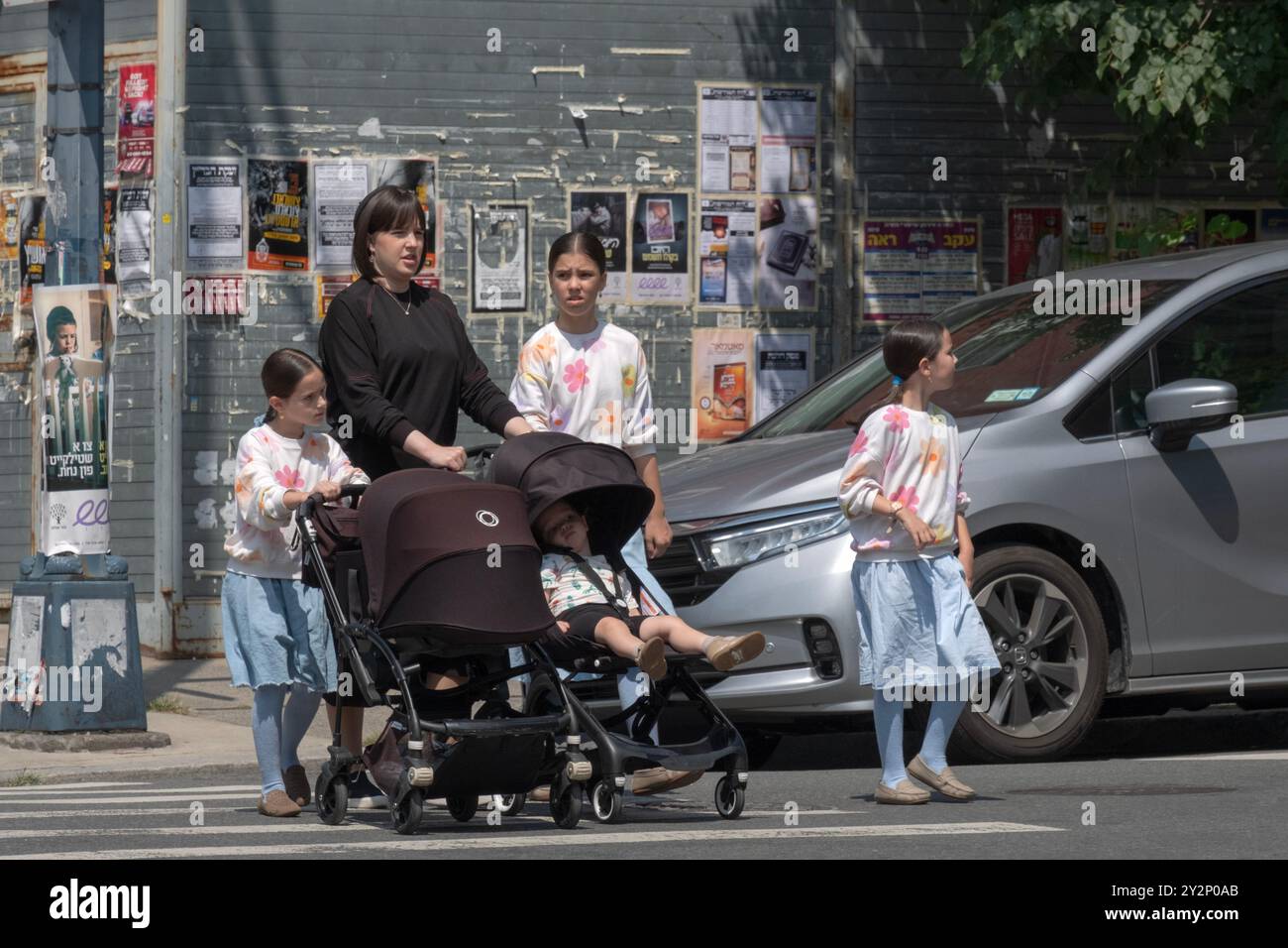 Una madre ebrea ortodossa con 4 bambini e 3 vestiti allo stesso modo attraversa una strada a Williamsburg, Brooklyn, New York Foto Stock