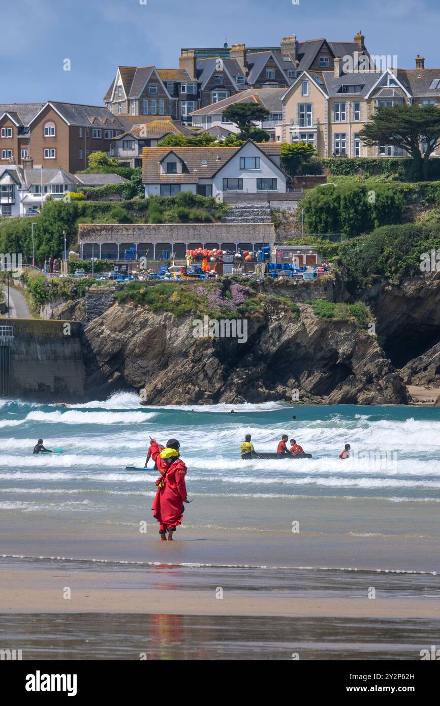 Un bagnino della Royal National Lifeboat Institution della RNLI, in servizio sulla riva, osservando i surfisti principianti che tengono una lezione di surf in mare a Towan Foto Stock