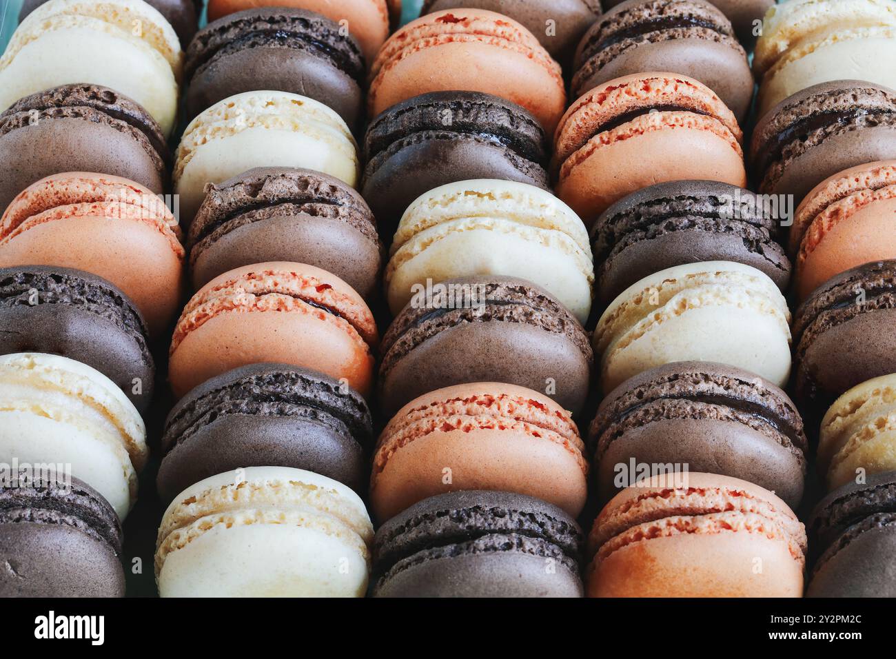 Vista dal tavolo di una serie di macaron francesi aromatizzati. Bianco, latte e cioccolato fondente con aromi arancioni. Foto Stock