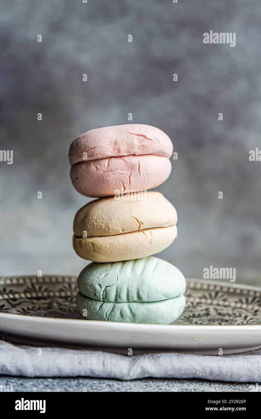 Un'elegante esposizione di tre macaron color pastello, rosa, beige e verde, impilati in modo ordinato l'uno sull'altro su un piatto decorativo con un intricato detai Foto Stock