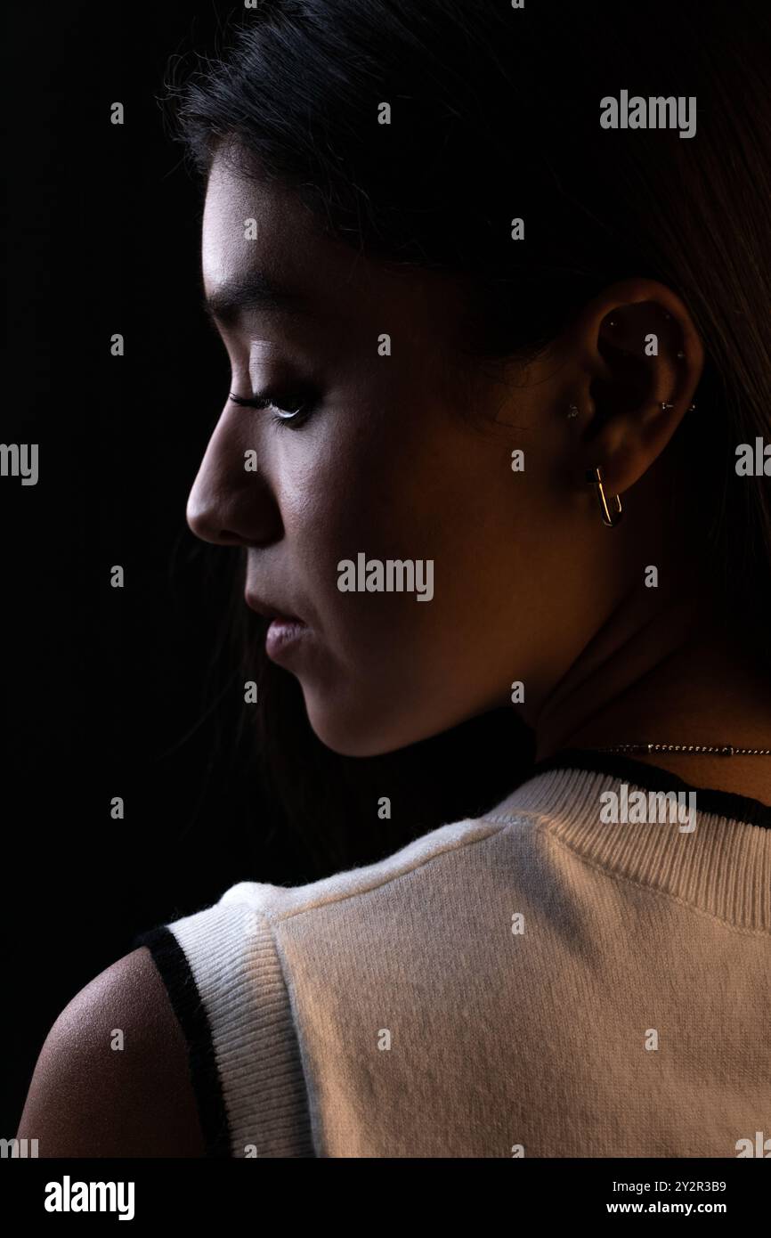 Una modella messicana femminile, ritratta in un primo piano lunare, guarda verso il basso con un'espressione contemplativa. L'immagine viene illuminata per evidenziare la sua plancia Foto Stock