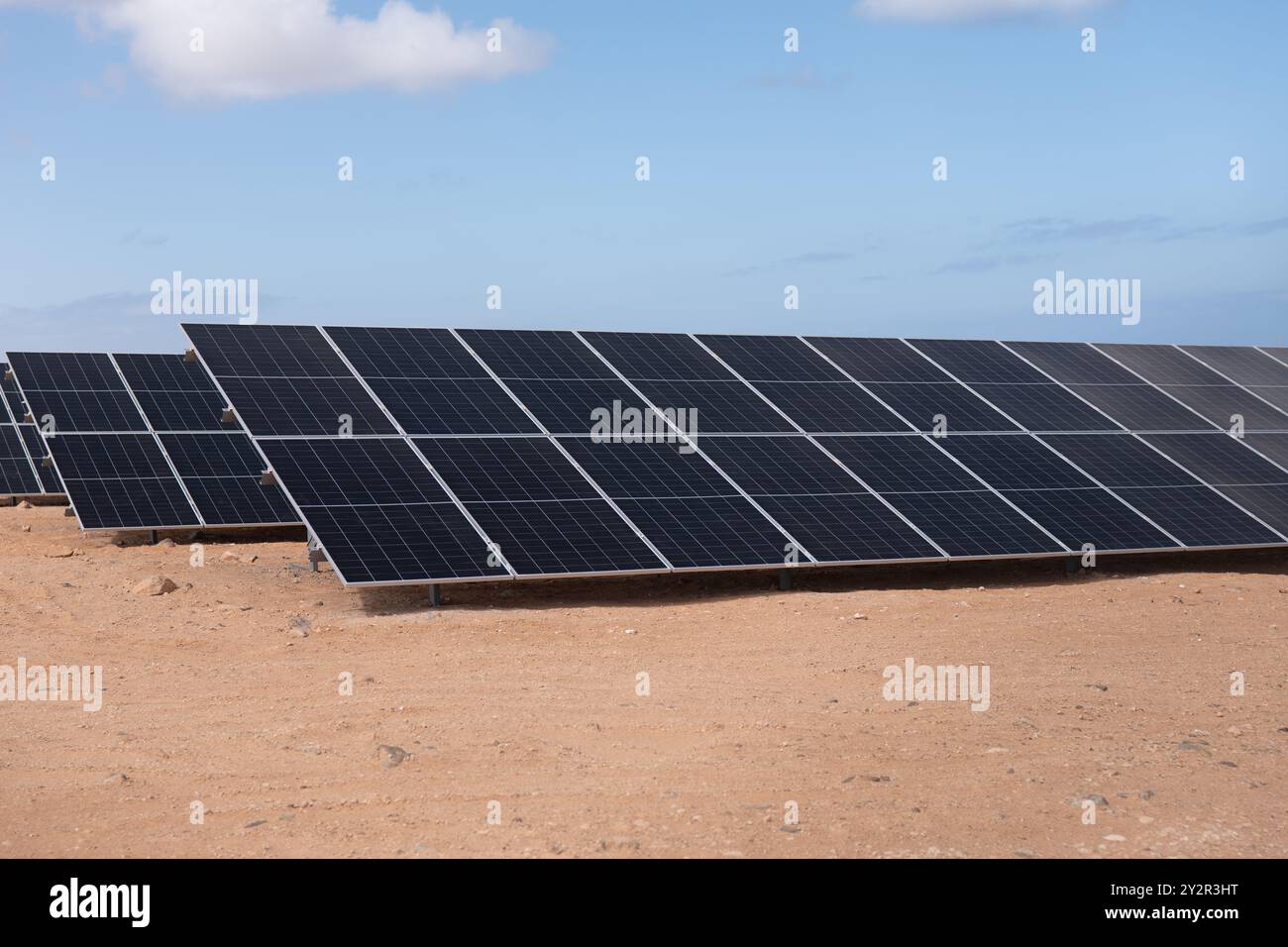 File di eleganti pannelli solari scuri si estendono su un paesaggio arido e sabbioso, sfruttando la luce del sole sotto un cielo blu limpido per generare energia pulita e rinnovabile Foto Stock