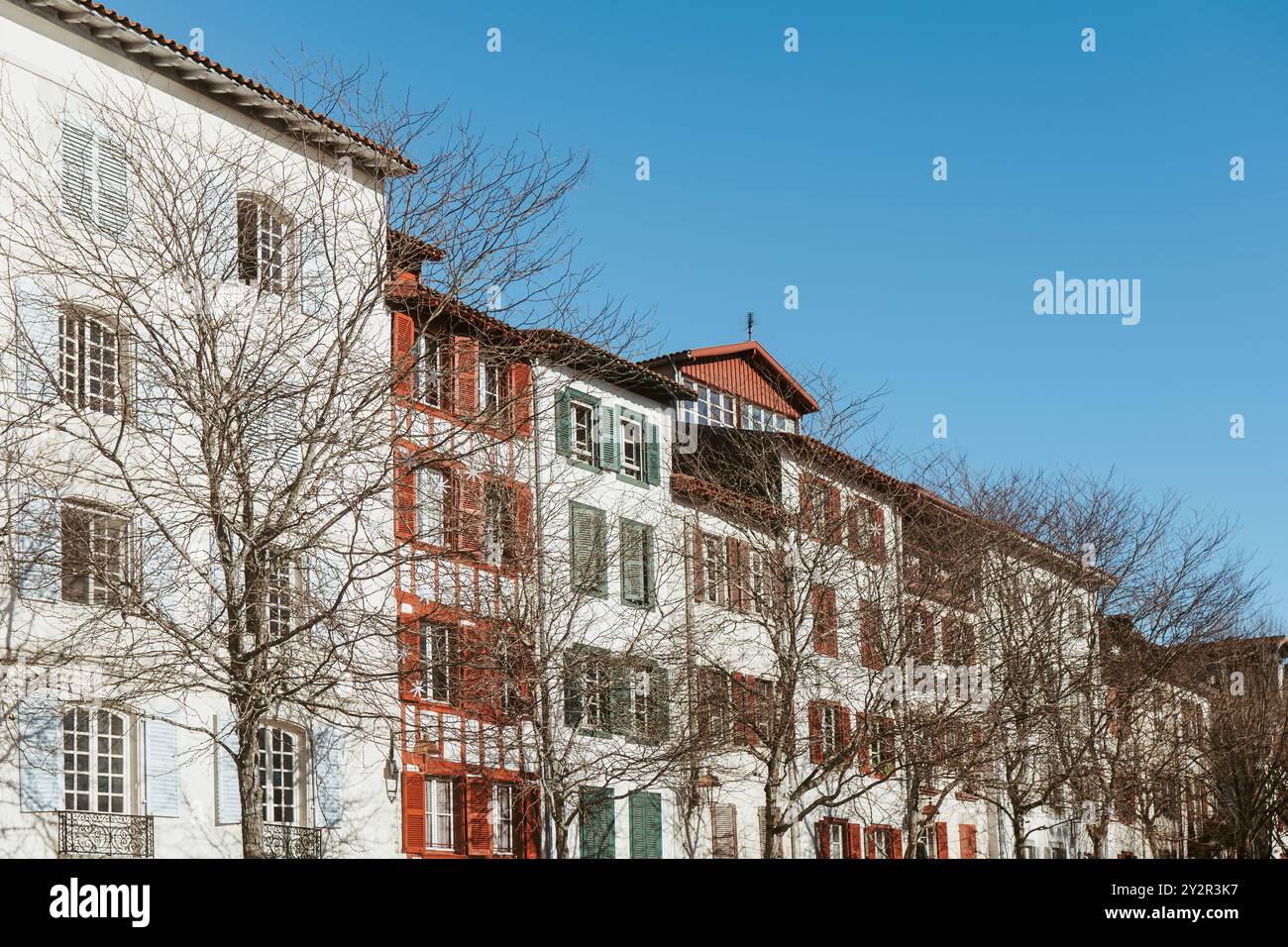 Una fila di tradizionali case basche a Bayonne, con le loro tipiche facciate bianche e le persiane rosse, sotto un cielo azzurro. Foto Stock
