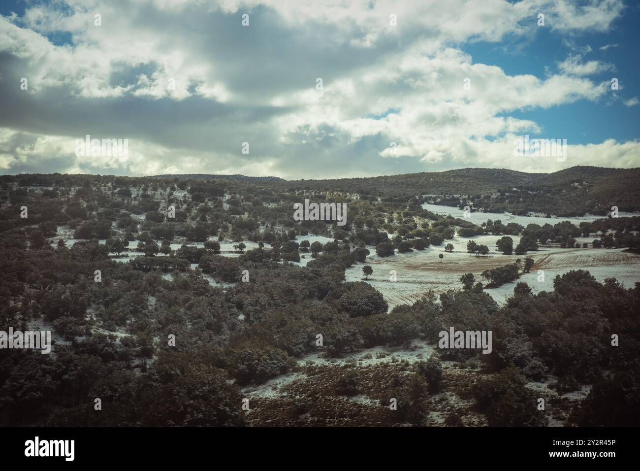 Un paesaggio sereno che presenta dolci colline punteggiate di alberi, parzialmente ricoperte da una leggera spolveratura di neve, sotto un cielo pieno di spettacolari nuvole Foto Stock