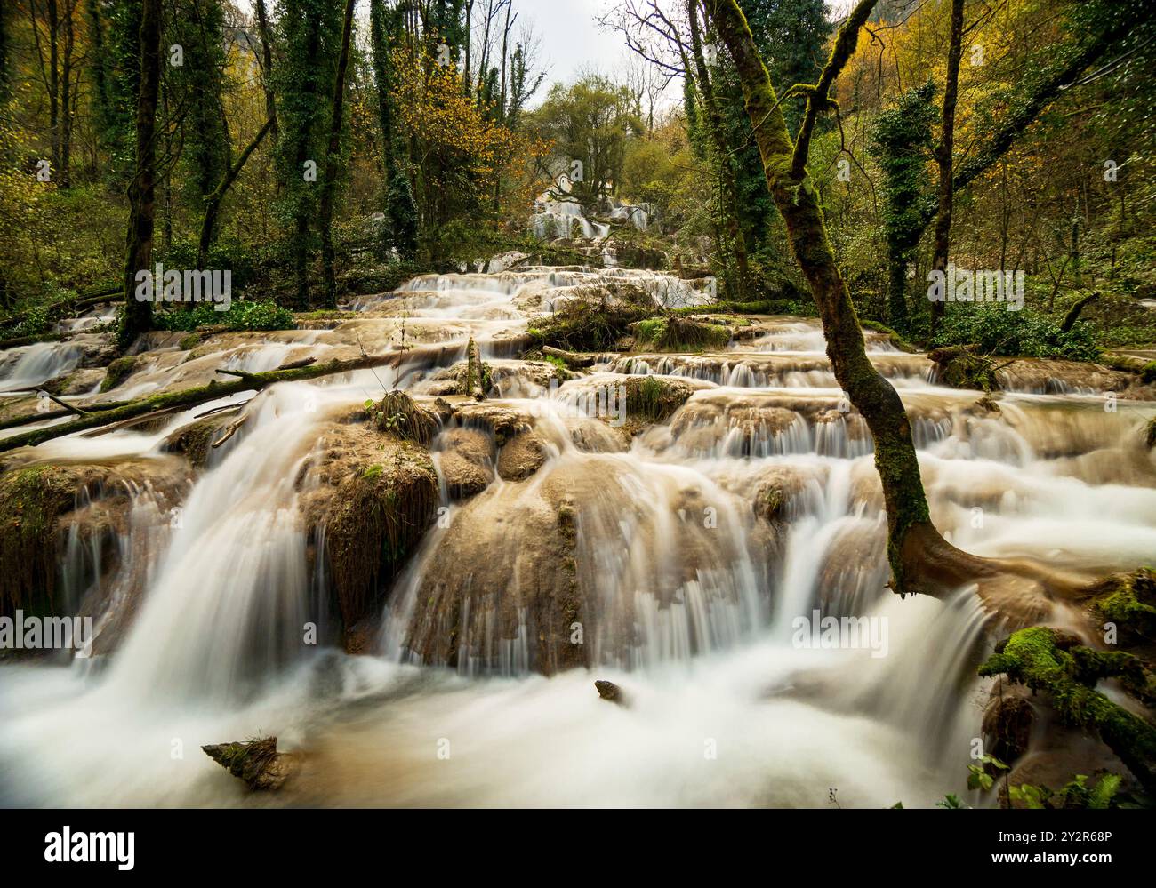 La lussureggiante vegetazione circonda la Cascade des TUFS, una tranquilla cascata del Giura francese, catturata con una lenta velocità dell'otturatore per un'acqua liscia Foto Stock
