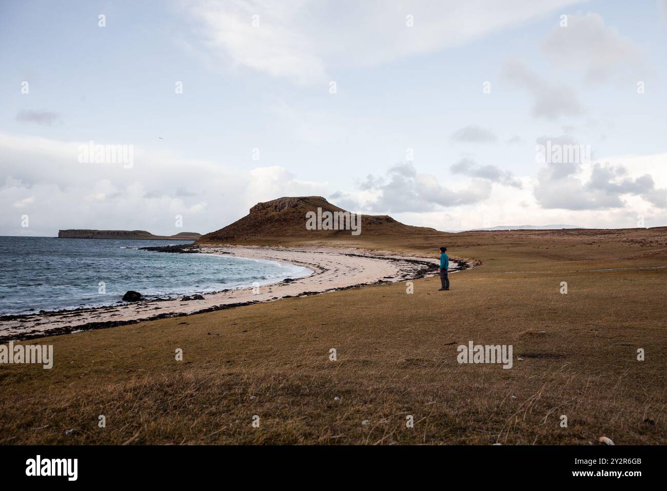 Vista laterale di un uomo irriconoscibile che esplora le tranquille spiagge delle Highlands scozzesi, catturando la dura bellezza del paesaggio durante l'inverno Foto Stock