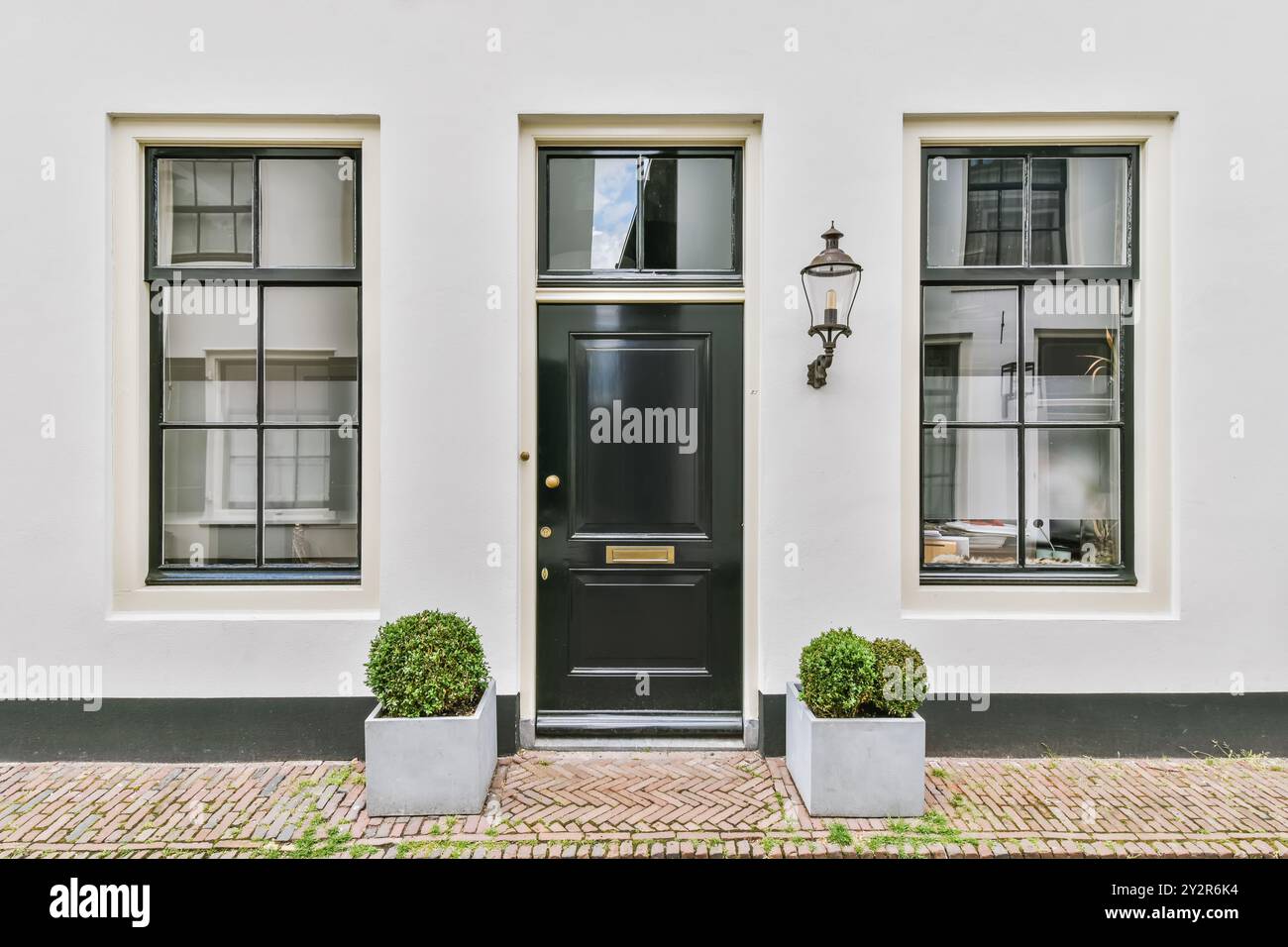 Una classica entrata europea della casa cittadina presenta una porta nera fiancheggiata da finestre bianche e piante in vaso. Foto Stock